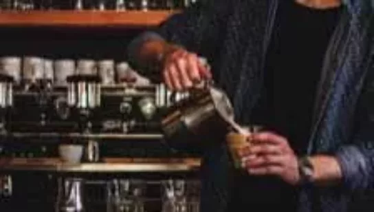 close up of a barista pouring milk into a glass of coffee