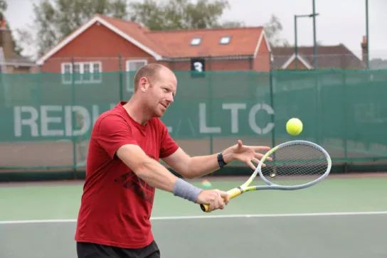 Man in red t shirt hitting a tennis ball